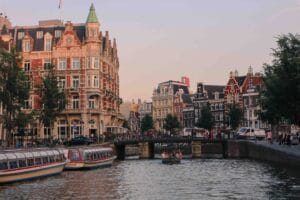 Zicht op de Amsterdamse grachten tijdens de schemering, met historische gebouwen en bruggen op de achtergrond