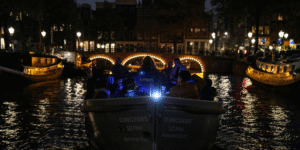 Verlichte bruggen en weerspiegelingen tijdens een nachtelijke rondvaart door Amsterdam.