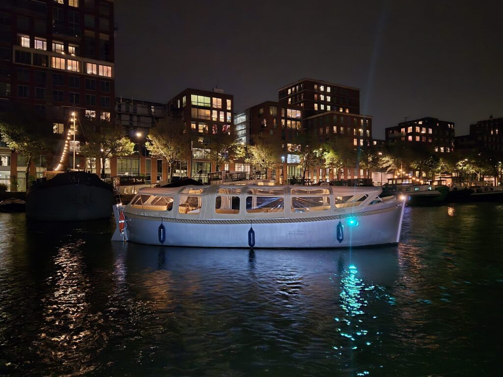 Overdekte KINboat vaart door de verlichte grachten tijdens het Amsterdam Light Festival, met warme drankjes aan boord en uitzicht op lichtkunst.