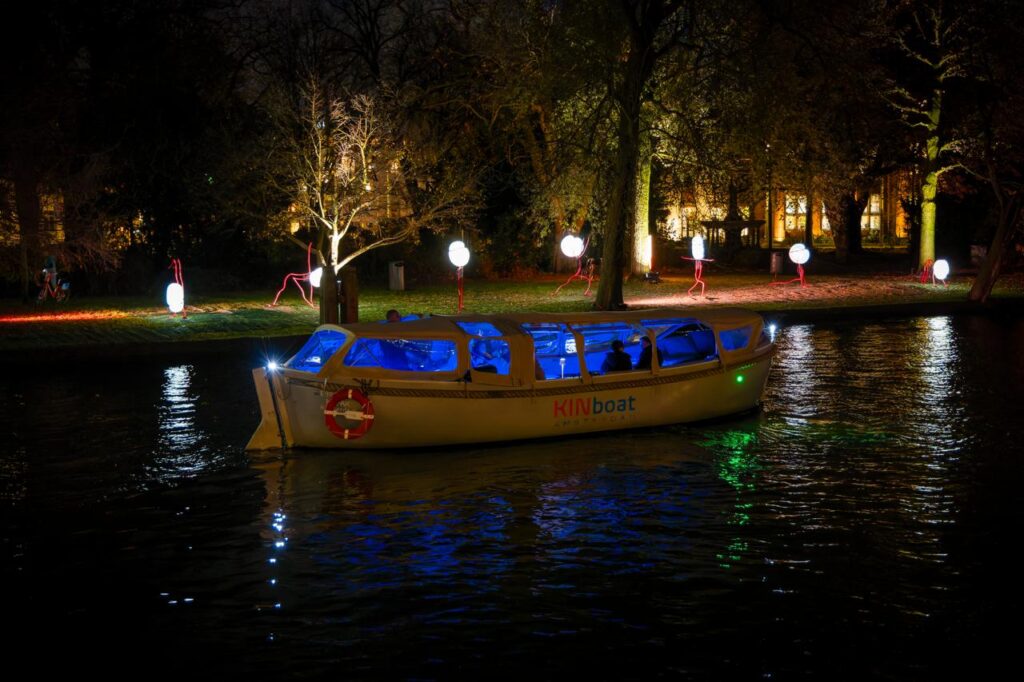 Overdekte KINboat die langs lichtinstallaties en verlichte bomen vaart tijdens het Amsterdam Light Festival.