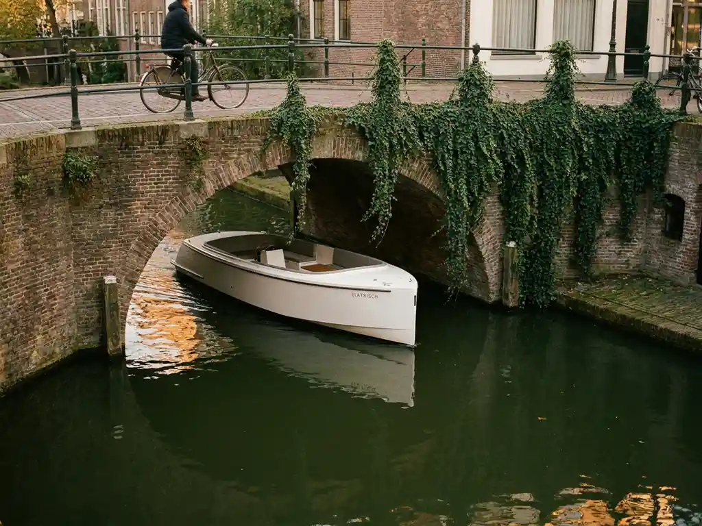 White electric boat gliding through a narrow Utrecht canal, flanked by ivy-draped brick bridges and golden afternoon reflections on still green water.