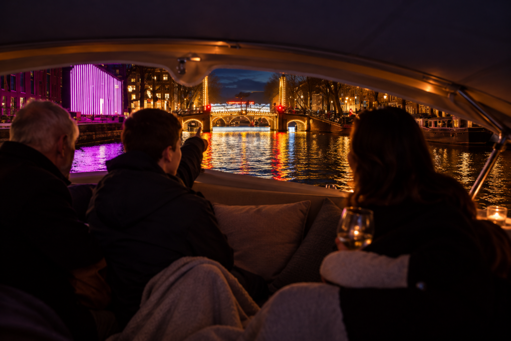 Gasten kijken vanuit een overdekte boot naar de verlichte Magere Brug en lichtkunst tijdens Amsterdam Light Festival