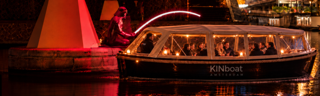 Overdekte KINboat sloep vaart langs een lichtkunstwerk onder een rood verlichte brug tijdens Amsterdam Light Festival